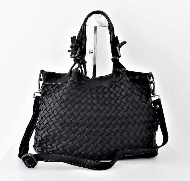 Pu&ograve; includere: Borsa a mano in pelle nera intrecciata con manico superiore e una lunga tracolla regolabile.