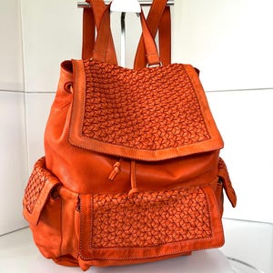 Peut inclure: Sac à dos en cuir orange avec un motif géométrique tissé sur le rabat et les poches avant. Il possède des bretelles réglables et une fermeture à cordon. Le sac est en cuir lisse et durable.