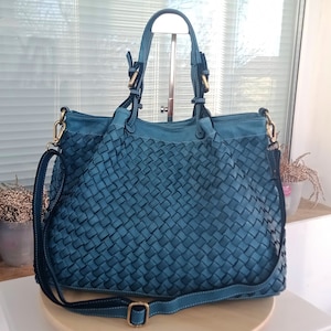 Pu&ograve; includere: Una borsa tote in pelle intrecciata blu turchese con una tracolla lunga e due manici superiori. La borsa ha un motivo intrecciato e accessori dorati.