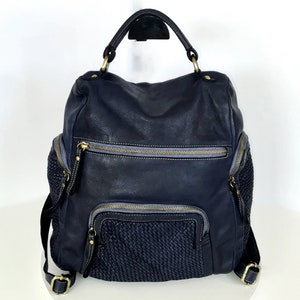 May include: A black leather backpack with a woven detail on the front. The backpack has a top handle and adjustable straps. It has multiple pockets and zippers.