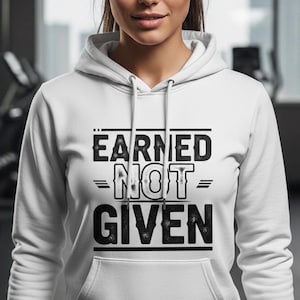 Peut inclure: Un sweat-shirt à capuche blanc avec le texte "EARNED NOT GIVEN" en noir. Le sweat-shirt a une poche avant et une capuche à cordon. La personne sur l'image est dans une salle de sport.