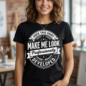 May include: A black short-sleeved t-shirt featuring a white graphic design with the text "DOES THIS SHIRT MAKE ME LOOK Professionally DEVELOPED" enclosed in a circular emblem with laurel leaves, stars, and decorative banner elements.