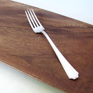 May include: A silver-colored metal fork with four tines and a smooth, tapered handle. The fork features a polished, reflective finish and a simple, clean design with a slightly pointed end on the handle, showcasing a classic, functional aesthetic.
