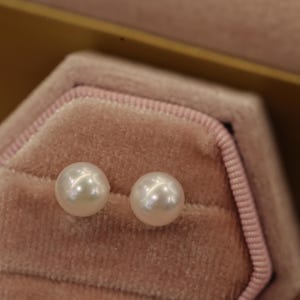 May include: A pair of white pearl earrings in a pink velvet jewelry box.