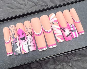 May include: A set of ten long, coffin-shaped false nails with a matte finish. Each nail features a unique Halloween-themed design, including ghosts, spiderwebs, and mummy wraps, in pink, white, and black colors.