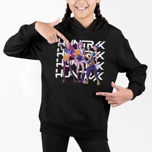 Könnte beinhalten: Schwarzer Kapuzenpullover mit einer Grafik von drei stilisierten Figuren in farbenfrohen Outfits und dem Wort "HUNTRX" in weißen Blockbuchstaben. Die Figuren sind in verschiedenen Posen. Der Hoodie hat eine Kängurutasche und eine Kapuze mit Kordelzug.