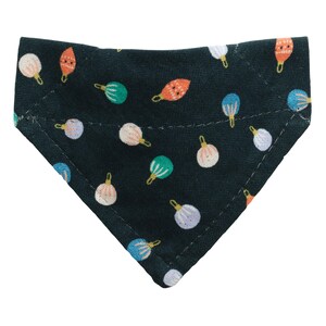 Könnte beinhalten: Ein dunkelgrünes, dreieckiges Haustier-Bandana mit einem sich wiederholenden Muster aus farbenfrohen, stilisierten Ornamenten. Die Ornamente sind in den Farbtönen Orange, Blau, Grün, Rosa und Weiß gehalten, jedes mit einem goldfarbenen Aufsatz. Das Bandana ist aus Stoff.