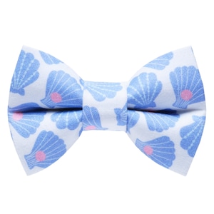 May include: A blue and white bow tie with a seashell pattern. The bow tie has a white background with blue seashells and pink centers.