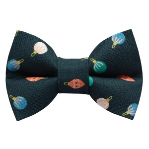 Könnte beinhalten: Eine dunkelblaue Fliege mit einem sich wiederholenden Muster aus bunten Weihnachtskugeln. Die Ornamente sind in Orange, Rosa, Grün und Blau gehalten. Die Fliege ist aus einem strukturierten Stoff gefertigt.