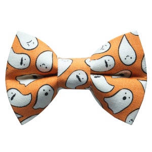 May include: A Halloween-themed bow tie featuring a repeating pattern of white cartoon ghosts on an orange background. The bow tie is pre-tied and ready to wear. Perfect for adding a festive touch to any outfit.