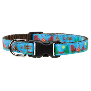 May include: A blue cat collar with a camping themed print featuring tents, campfires, and trees. The collar has a brown adjustable strap and a black plastic buckle.