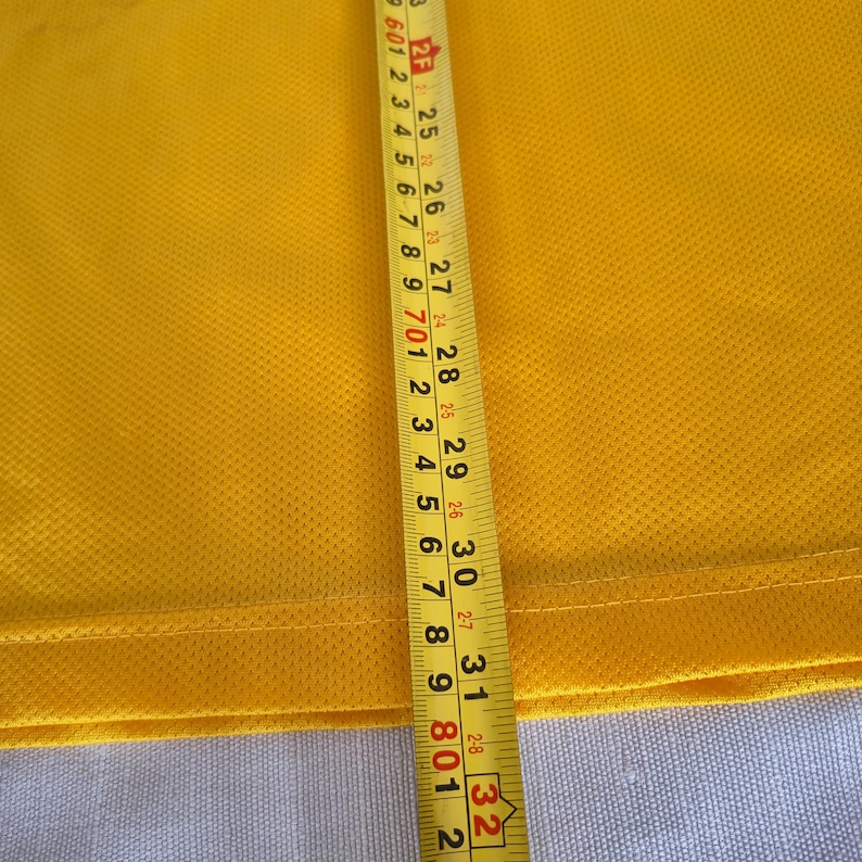 Pu&ograve; includere: Primo piano di un tessuto giallo con un metro a nastro. Il nastro mostra misure da 63,5 cm a 81,3 cm. Il tessuto ha una superficie strutturata.