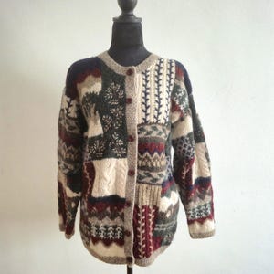 以下が含まれることがあります： ベージュ、バーガンディ、グリーン、ネイビーブルーの色合いのパッチワークカーディガン。丸いネックライン、ボタン留めのフロント、ケーブルニットやフローラルデザインなど、さまざまな模様のパネルが特徴です。マネキンに飾られたセーター。