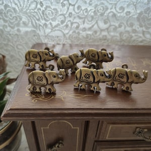 Peut inclure: Ensemble de poignées de tiroir antiques en forme d'éléphant en laiton. Les boutons d'éléphant sont disposés sur une surface en bois, mettant en valeur leur design détaillé et leur attrait vintage. Les boutons d'éléphant ont un motif floral sur leur corps.