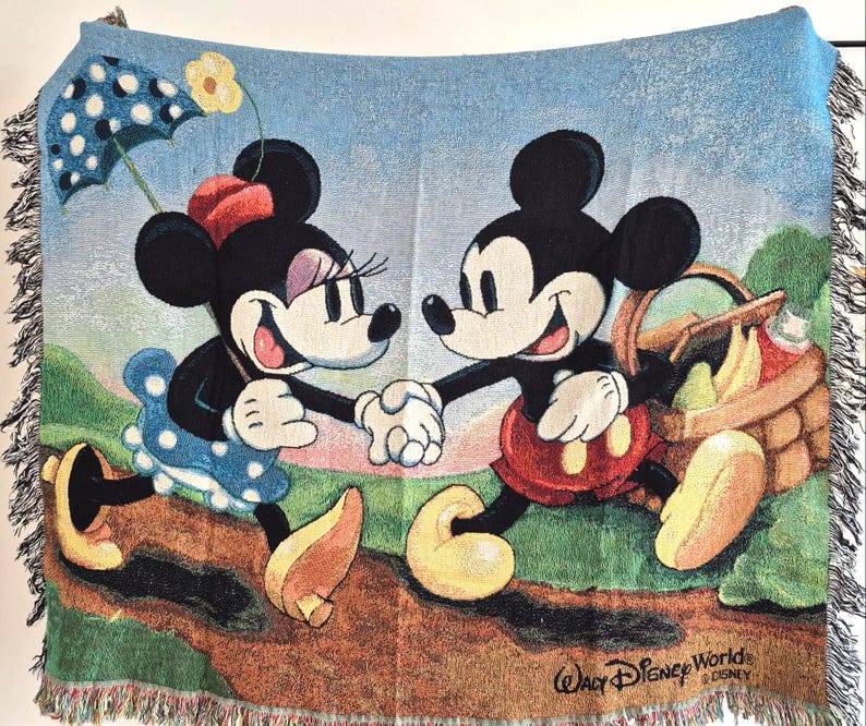 May include: A woven throw blanket featuring Mickey and Minnie Mouse holding hands, with a picnic basket and umbrella. The blanket has a light blue background with a fringed edge and the text "Walt Disney World" at the bottom.