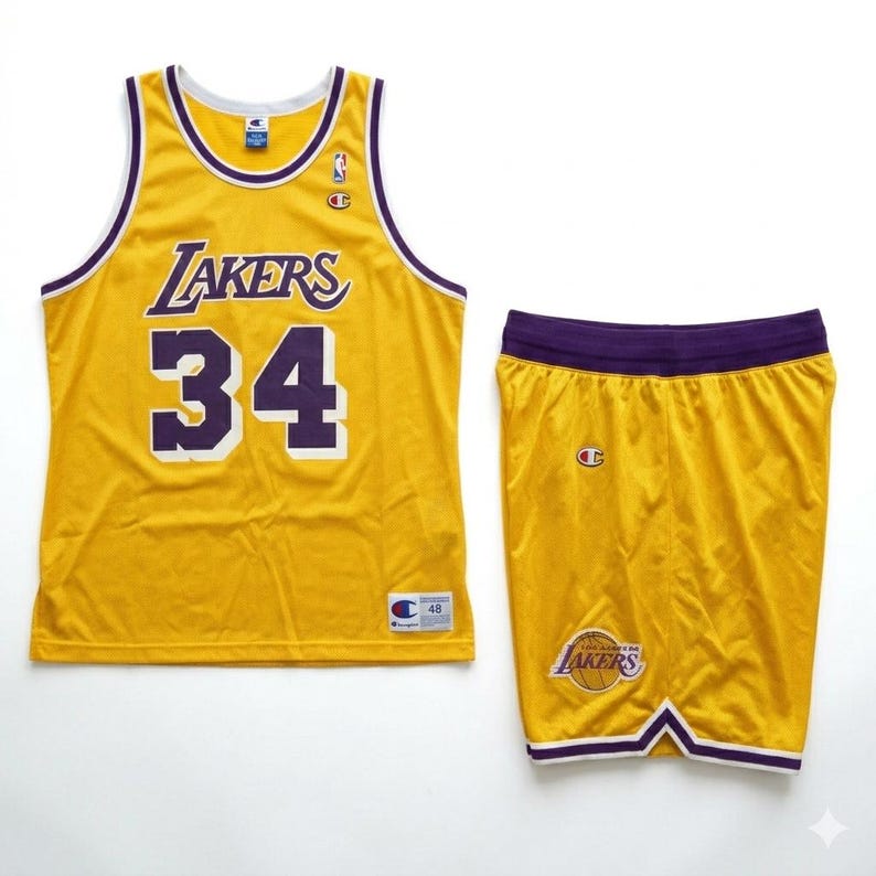 Pu&ograve; includere: Un completo da basket giallo composto da maglia e pantaloncini. La maglia presenta la scritta "Lakers" e il numero "34" in viola. I pantaloncini hanno il logo dei Lakers e un girovita viola. Il completo &egrave; prodotto da Champion.