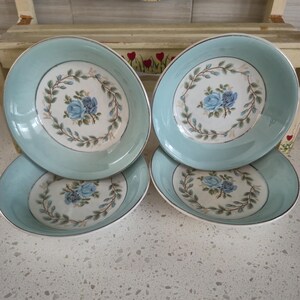 May include: Four vintage light blue bowls with a floral design. Each bowl has a central blue rose surrounded by a wreath of green leaves. The rims are trimmed with silver, adding a touch of elegance to the tableware.