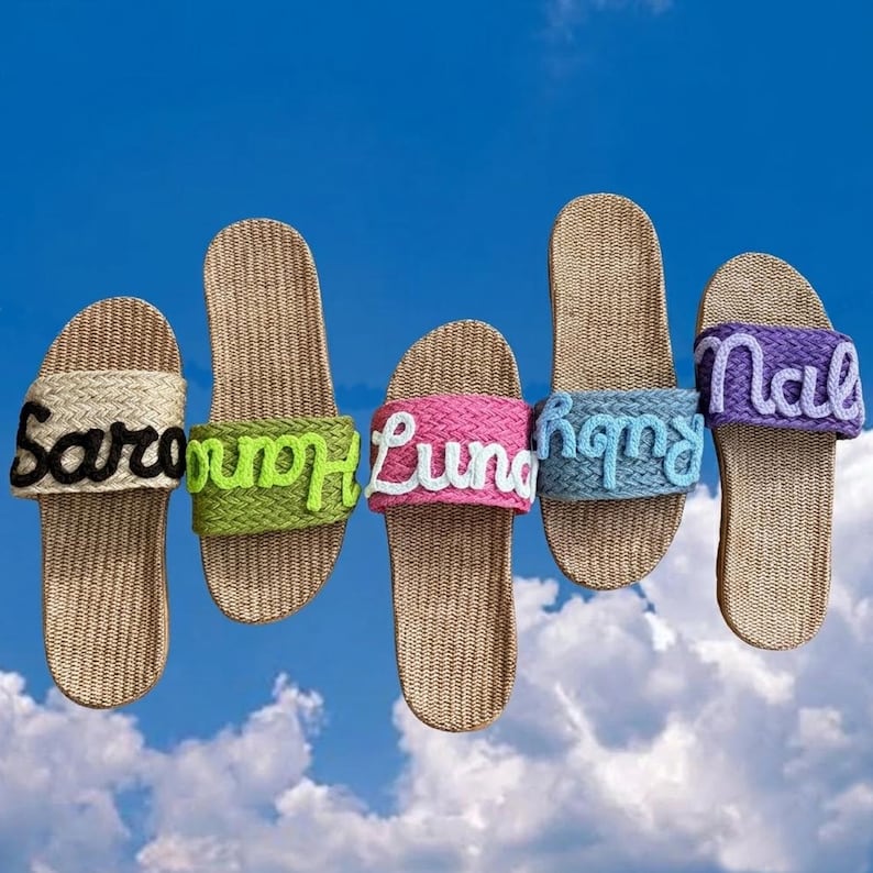 K&ouml;nnte beinhalten: F&uuml;nf Paar Schlupfsandalen mit gewebten beigen Fu&szlig;betten und geflochtenen Riemen in Beige, Limettengr&uuml;n, Pink, Hellblau und Lila. Jeder Riemen ist mit einem in Kontrastfarbe gestickten Namen versehen: Saro, Hana, Luna, Ruby und Nala.