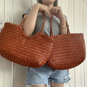 K&ouml;nnte beinhalten: Zwei gewebte Leder-Tragetaschen in einem warmen Braunton. Die Taschen haben ein Korbgeflecht-Design und geflochtene Griffe. Die Taschen sind in Gr&ouml;&szlig;e und Form &auml;hnlich, mit einer gebogenen Oberkante.