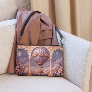 Può includere: Borsa a tracolla con un design stravagante a mongolfiera. La borsa presenta un pallone viola adornato con rose rosa, ambientato su un cielo notturno con luna piena e nuvole. Ha una tracolla nera e poggia su un divano chiaro.