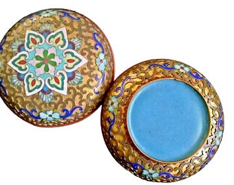 May include: A round, gold-colored box with blue and white enamel floral designs. The lid is open, revealing a blue interior.
