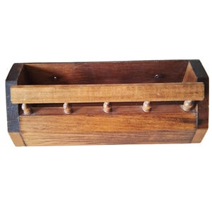 May include: A wooden wall-mounted mail organizer with a rectangular shape. The organizer is made of light and dark brown wood, with a horizontal bar and decorative wooden knobs. The design is simple and rustic.