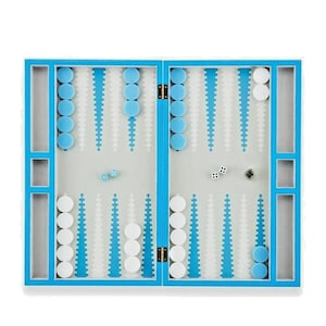 May include: A backgammon board with a white playing surface, blue and white game pieces, and dice. The board has a blue border and a hinged design for easy storage. The game is set up and ready to play.
