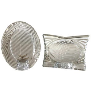 May include: Two clear glass picture frames. One is oval with a wavy pattern and the text "Friend to Friend". The other is square with an oval center and a similar design. Both frames are empty.