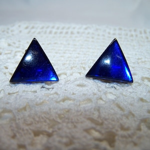 May include: A pair of triangular stud earrings. Each earring is a vibrant, glossy blue, shaped as a triangle. The earrings are set against a white, textured background, highlighting their bold color and geometric design. These earrings are a striking accessory.