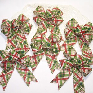 May include: Six plaid Christmas bows with gold trim. The bows are red, green, and white plaid with gold glitter accents. The bows are tied with a gold ribbon.