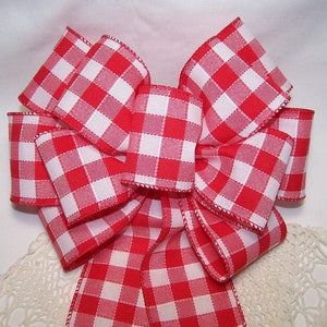May include: A large red and white gingham bow. The bow is made of a thick, woven fabric with a checkered pattern.