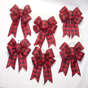 May include: Six red and black buffalo plaid bows with wired tails. The bows are tied with a black wire and are ready to be used for decorating.