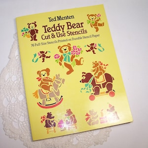 May include: A yellow stencil book titled "Teddy Bear Cut & Use Stencils" by Ted Menten. The cover features brown teddy bear illustrations with flowers and other designs. The book contains 76 full-size stencils printed on durable stencil paper.