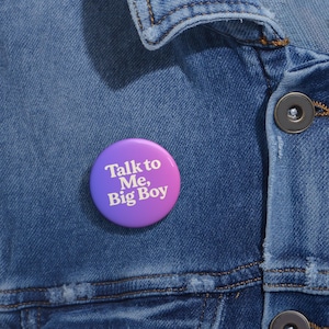 Op de afbeelding: Een paarse en roze knop met de tekst "Talk to Me, Big Boy" in wit.