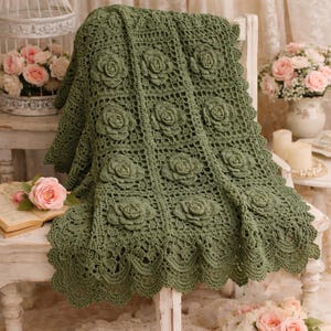 Peut inclure: Une couverture au crochet vert sauge avec des motifs de roses en relief. La couverture est drapée sur une chaise blanche, mettant en valeur son design floral complexe et ses bords festonnés. La couverture faite à la main ajoute une touche vintage.