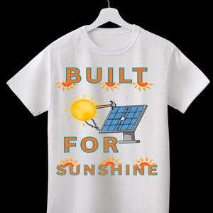 Puede incluir: Una camiseta blanca de manga corta con un gráfico de un sol amarillo usando un martillo y alicates en un panel solar azul. El texto BUILT FOR SUNSHINE está impreso en azul con bordes naranjas, acompañado de pequeños iconos de sol naranjas.