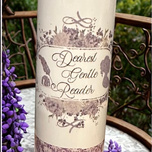 May include: A cylindrical tumbler with a purple damask pattern and the words "Dearest Gentle Reader." The tumbler has a cream-colored center with floral and silhouette accents. The background includes purple flowers and a decorative table.