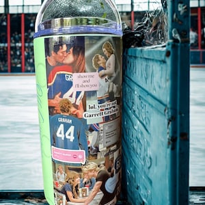 May include: A cylindrical tumbler with a clear lid featuring a collage of images and text including "show me and I'll show you", "lol. you're not Garrett Graham", "GRAHAM 44", and "OFF CAMPUS". The design includes scenes of people and hockey-themed graphics.