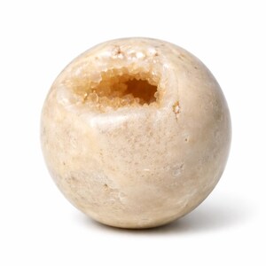 May include: A spherical, beige geode with a hollowed-out center revealing a cluster of small, sparkling crystals. The geode has a smooth, polished exterior and is set against a white background.