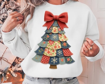Può includere: Felpa bianca con un design a forma di albero di Natale. L'albero è realizzato in tessuto a strati con vari motivi, tra cui disegni floreali e fiocchi di neve, sormontato da un fiocco rosso. Il tronco dell'albero è marrone.