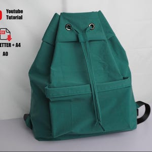以下が含まれることがあります： 2つのフロントポケットと黒いショルダーストラップが付いた、ティール色の巾着バックパック。バッグには金属製のアイレットと巾着開閉部があります。画像には「Youtube Tutorial」と「US_LETTER + A4 A0」の文字も含まれています。