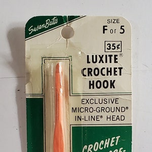 May include: An orange Luxite crochet hook in its original packaging. The green and white packaging features the brand name "Susan Bates" and text that reads "Crochet with ease-smoother, faster." The hook is size F or 5.