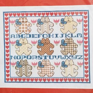 May include: A Country counted cross stitch kit featuring a teddy bear sampler. The design includes teddy bears, letters of the alphabet, and floral accents. Finished size is 14 inches by 12 inches.