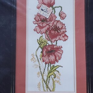 May include: A cross-stitch kit featuring a floral design of red poppies. The kit includes 100% cotton Aida cloth, floss, a graph, and a needle. The finished size is 7" x 16" (17.78 cm x 40.64 cm), matted size is 11" x 20" (27.94 cm x 50.8 cm). The kit is from Candamar Designs.