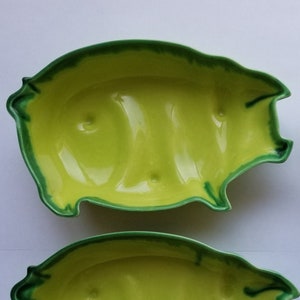 May include: Four ceramic serving dishes in the shape of a fish. The dishes are a bright yellow-green color with a darker green trim around the edges. The dishes are arranged in a square.