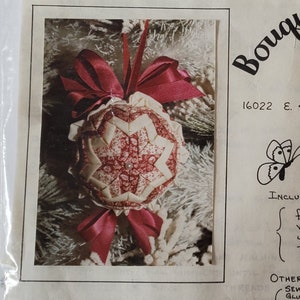 May include: A craft kit in a clear plastic bag. The kit includes fabric, velvet and satin ribbon, pearl pins, and a pattern. The packaging features a photo of a handmade Christmas ornament with a red bow and the text "Bouquets & Butterflies Creation".