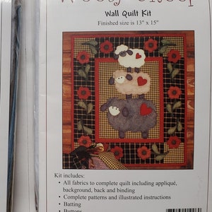 May include: Two wall quilt kits, one featuring owls and the other sheep. The "Owl Family" kit shows a tree with owls, a moon, and stars. The "Wooly Sheep" kit displays three sheep. Both kits are 13" x 15" when finished.