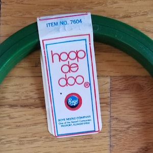 May include: A green plastic embroidery hoop with a metal screw and clasp. A white tag with red and blue text reads "hoop de doo" and "Boye". The hoop is 7 inches in diameter.