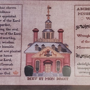 May include: Framed cross-stitch artwork featuring a red building with a steeple, text, and decorative elements. The text includes religious verses and the phrase "DIEV ET MON DROIT". The artwork is dated 1988.