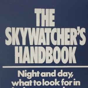 May include: A navy blue book titled "THE SKYWATCHER'S HANDBOOK" with white lettering. The book cover includes the text "Night and day, what to look for in the heavens above" and a series of moon phase illustrations. Author: Colin A. Ronan.